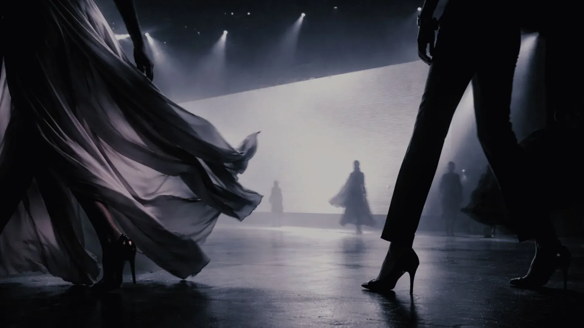 Models walk a misty, spotlit runway past a glowing LED wall.